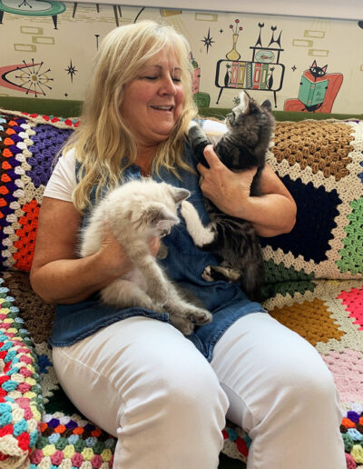 Visitor to the cat den cuddles two cats in her arms